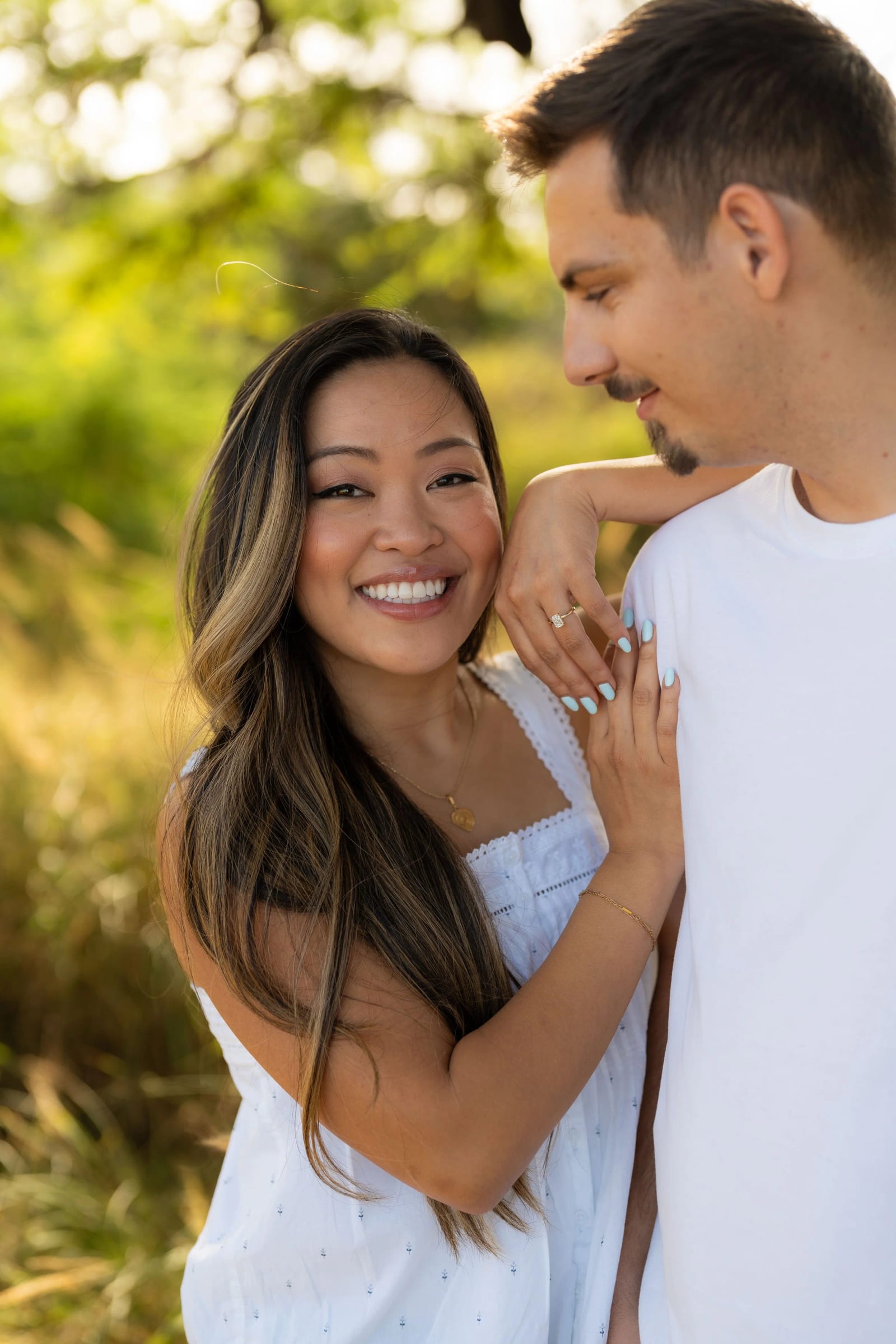 A couple laughing together among tall grass, her hand on his shoulder.