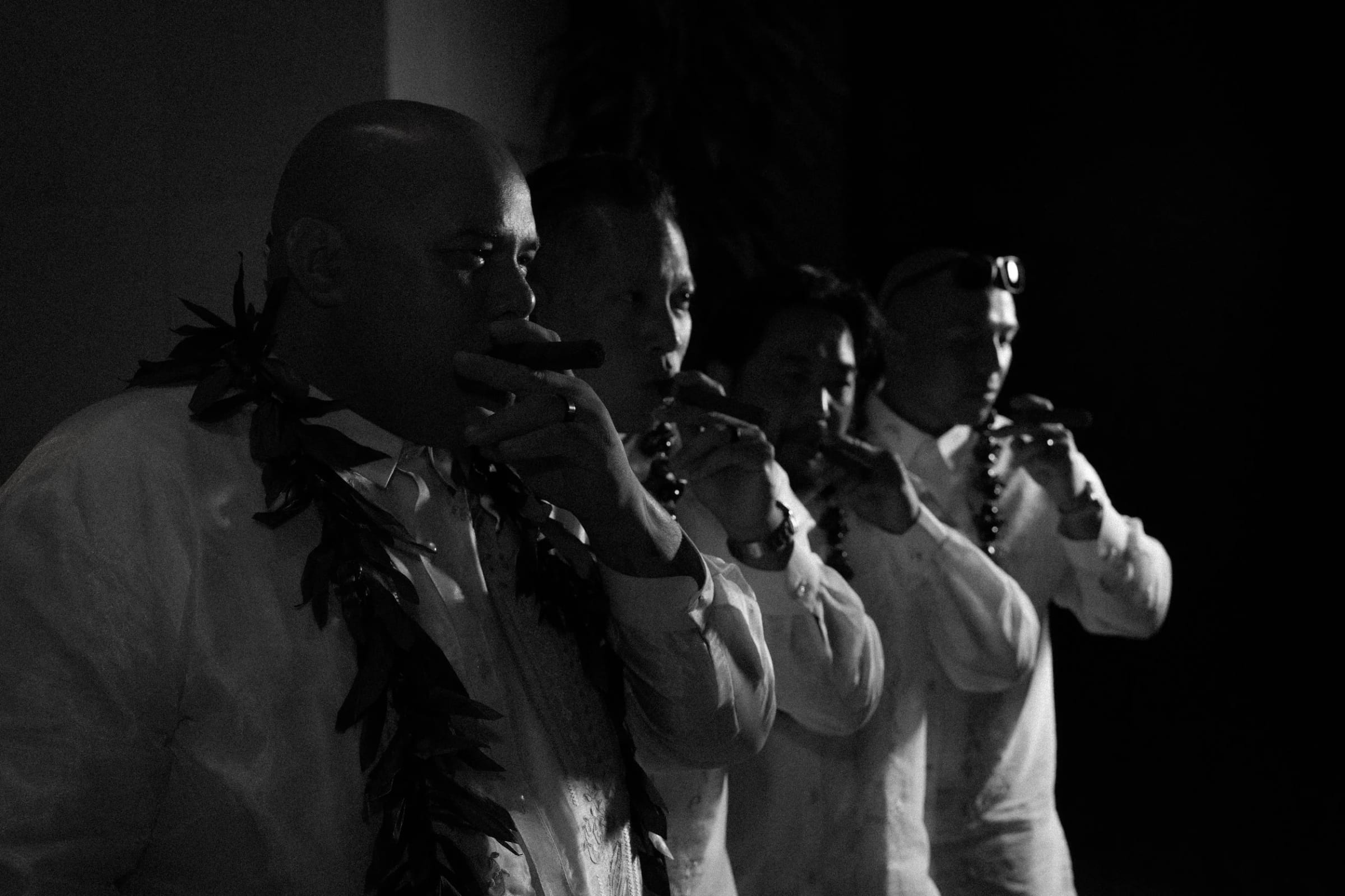 The groomsmen in lei raise their drinks together, in black and white.